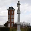 Stone monument featuring soldier on pedestal with clock tower in the background