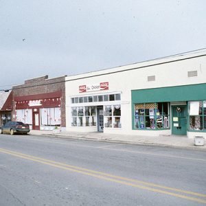 Street with single-story storefronts soda advertisements and car