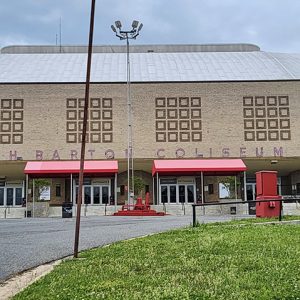 Multistory enclosed stadium building with red awnings and glass doors on parking lot