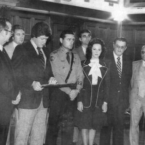 White man in suit giving an award to white man in police uniform with white men in suits and white woman standing with them