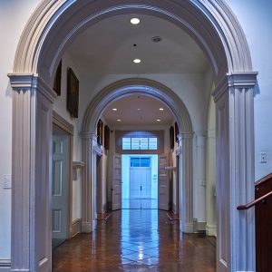 Looking down hallway with open doors and arches over tiled floor