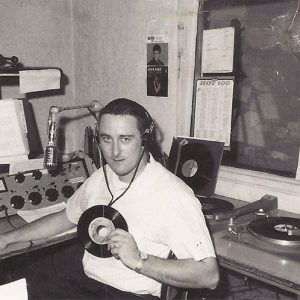 White man holding a vinyl record sitting in radio control room