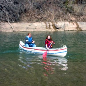 White man and woman navigating a river in a striped canoe