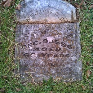 Broken stone marker laying in the grass "Rev. William C. Stout"