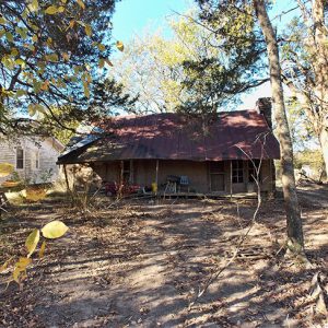 Single-story house with covered porch and rusted metal roof in forested area