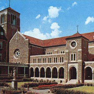 Multistory building with bell tower stained glass windows covered walk ways and clock tower surrounding courtyard with flowers and statue