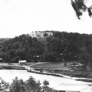 Three-story hotel on a hill with house and pond below it