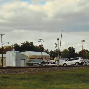 Train crossing with row of industrial buildings under cloudy skies