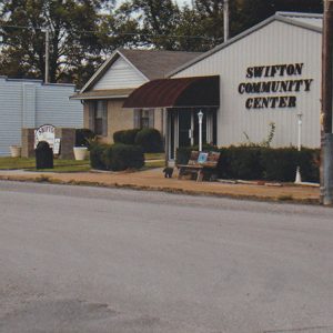 Single-story building with siding and awning over entrance on street with single-story buildings beside it