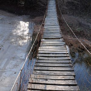 Looking across wooden bridge suspended over creek