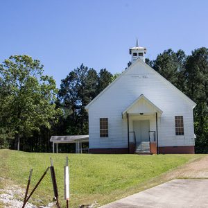 Single-story church building with A-frame roof with cupola and covered entrance on grass