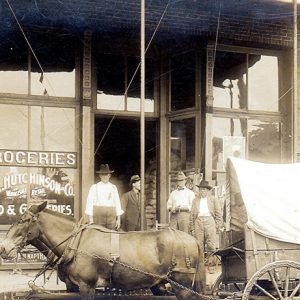 White men outside storefront with horse and covered wagon