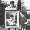 White man outdoors showing his daughter a painting of herself