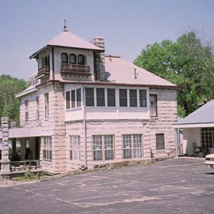 Multiple-story brick house with tower room and covered entrance near motel building and parking lot