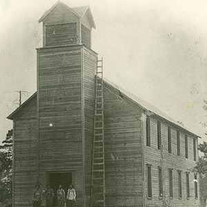 Four white men standing on steps of large wooden church building with bell tower