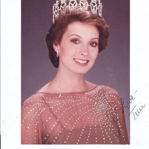 Young white woman with short hair smiling in tiara and dress with name and date below