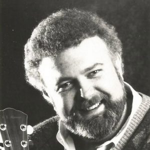 White man smiling in beard and sweater with guitar