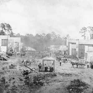 Storefronts on either side of dirt road with people and horses standing on it