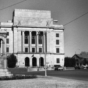 Multistory stone building with columns archways US flagpole and two-figure stone gazebo-style monument