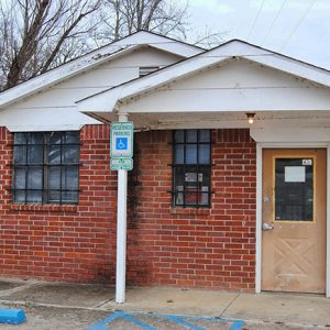 small single-story brick building with covered porch on parking lot