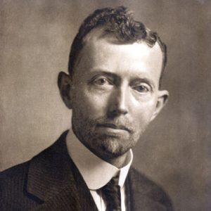 White man with curly hair and beard in suit and tie