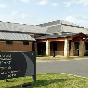 Brick building with covered entrance and hip roof on parking lot with sign outside