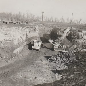 White workers and trucks parked above open pit with bull dozer loading dump truck at the bottom of it