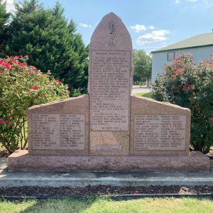 Engraved stone monument in flower bed with building behind it