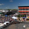 Crowded town square with tents and food stands in front of multistory buildings