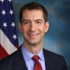 White man smiling in shirt and tie with American flag behind him