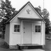 Small white building with pointed roof with awning and sign