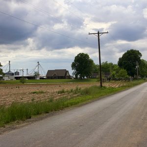 Rural road with farmland with silos and buildings on its left side