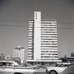 View from cars in the street looking at tall multistory building with piles of construction materials in front of it