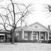 Single-story brick house with covered porch entrance with columns with trees in front