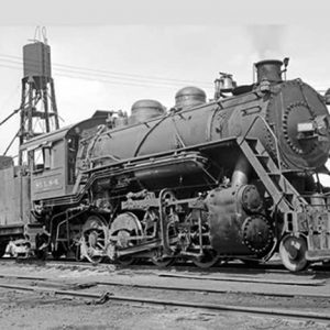 Steam locomotive on tracks with water tower in the background