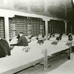 Two white men sitting on beds in barracks building