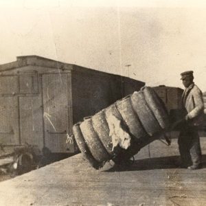 Man wheeling bale of cotton on a platform with train car nearby