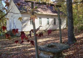 Side-view of single-story school house with wood siding and well in the foreground