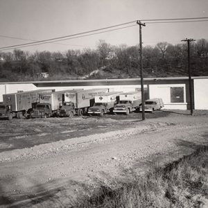 Fleet of trucks parked outside warehouse building on dirt road