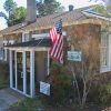 Close-up of single-story stone building with glass encased front entrance and flag