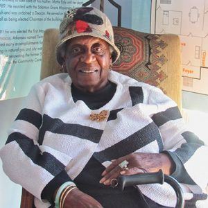 African-American woman with hat and cane sitting and smiling in chair