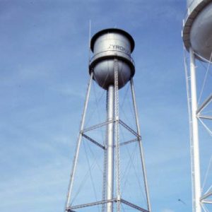 Two water towers and buildings inside fence