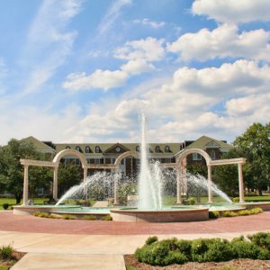 fountain surrounded on one side by three arches with multistory brick building in background