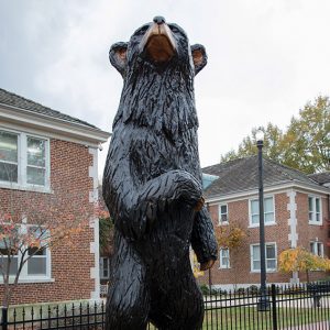 Close-up of bear statue on pedestal with multistory brick buildings behind it inside iron fence