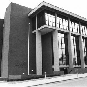 multistory brick building with tall paneled glass windows and street