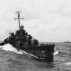 Naval ship underway at sea with two carrier ships in the background