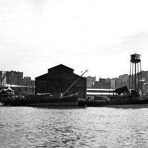 Boats moored at shipping depot with water tower and buildings in the background