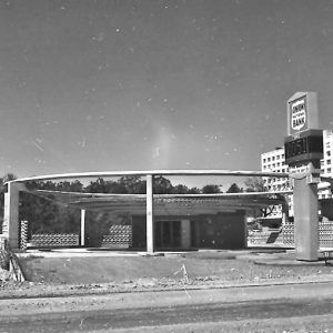 Single-story brick building surrounded by circular external structure with sign and multistory building in the background