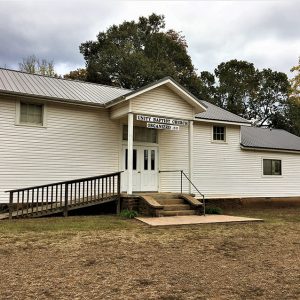 Single-story church building with hanging sign above front doors and wheelchair ramp