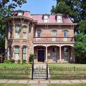 Multistory brick house with covered corner porch inside iron fence